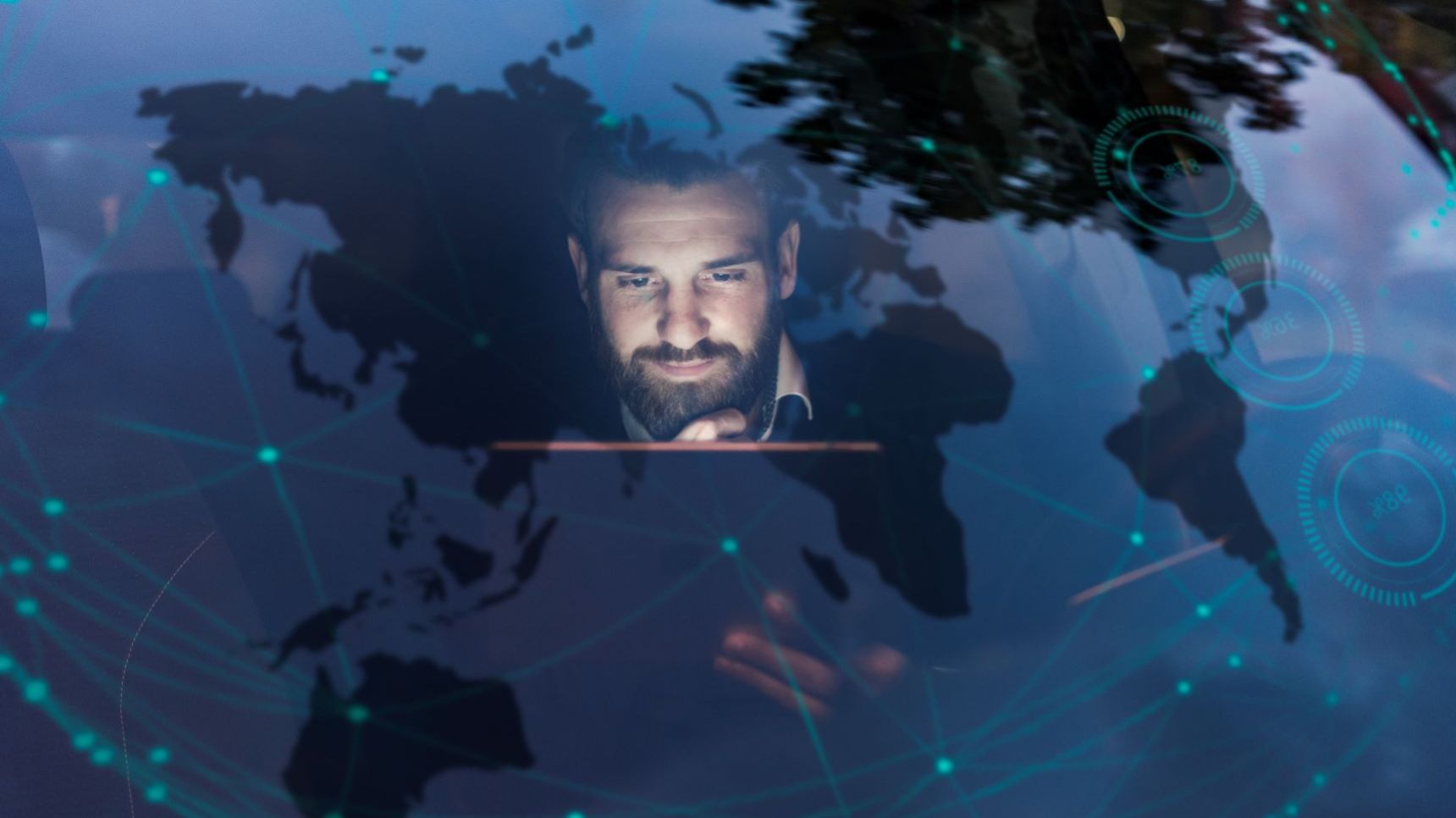 Ein Mann sitzt in einem Gebäude und schaut auf ein Tablet. Über das Bild sind digitale Grafiken einer Weltkarte und von Netzwerkverbindungen gelegt, wodurch ein futuristisches, globales Konnektivitätskonzept entsteht.